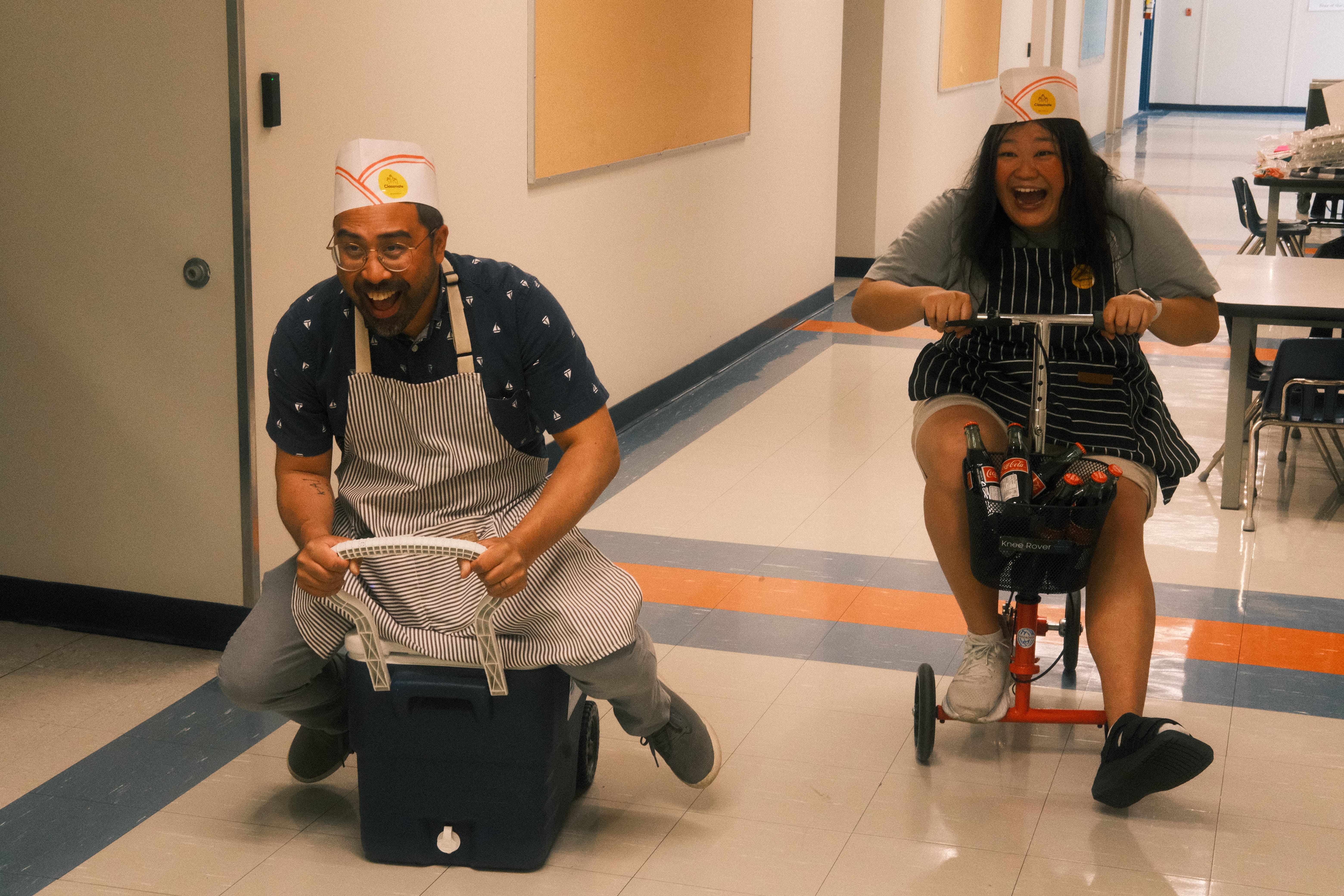 Carlo and Jen racing down a school hallway on a cooler and scooter.